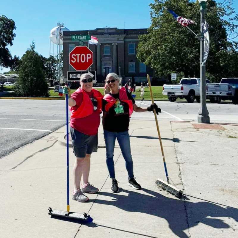 Two volunteers with push brooms sweeping a downtown street corner