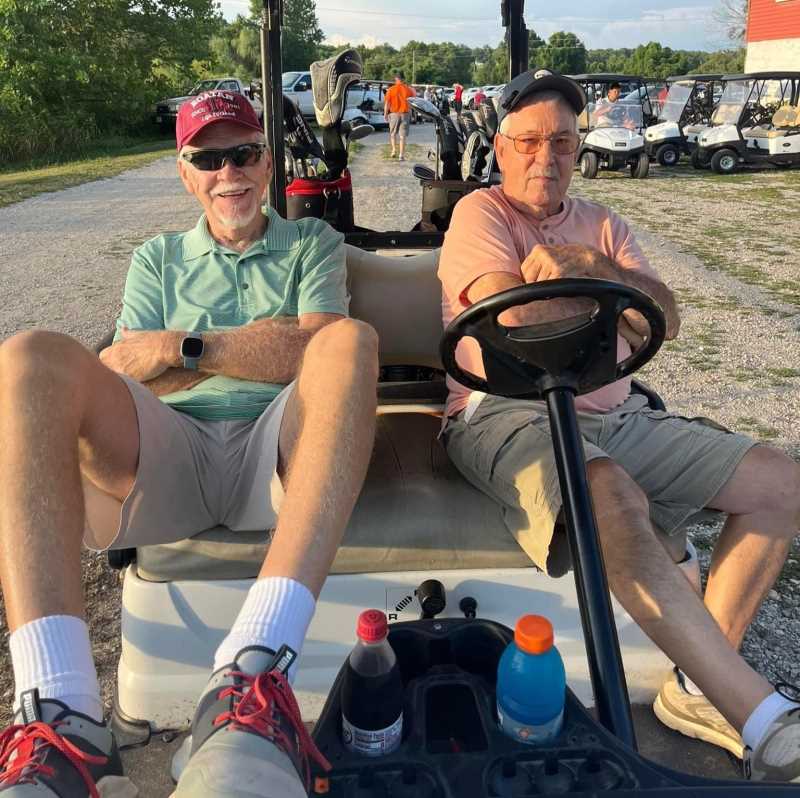 Two players relaxing in a golf cart at the Drives for Downtown golf tournament