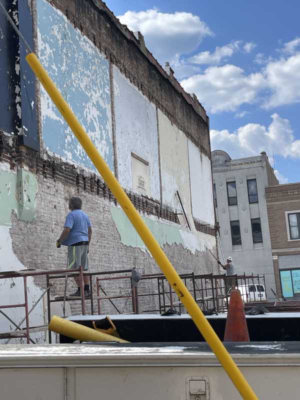 Worker on a lift restoring a faded mural on a historic brick wall downtown