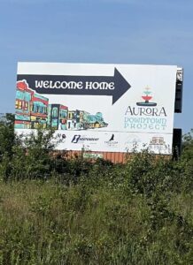 Welcome Home billboard featuring downtown mural artwork and the Aurora Downtown Project logo