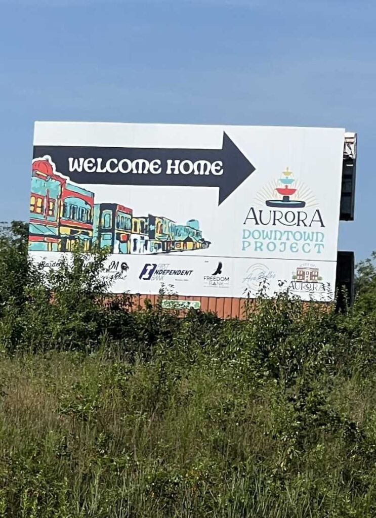 Welcome Home billboard featuring downtown mural artwork and the Aurora Downtown Project logo